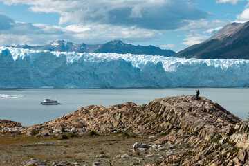 A man standing on the rock formation and taking a photo of the Perito Moreno Glacier