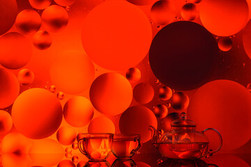 transparent glass teapot and cups with tea and drops on colorful background 