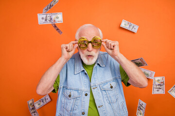 Photo of funky excited man pensioner dressed retro denim vest dollars eyewear winning jackpot isolated orange color background