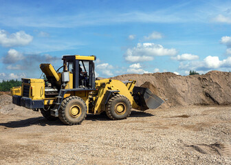 A big yellow tractor is carrying sand in a bucket. Front loader. Work on sand extraction in a quarry. Loading operations. A sand storage area.