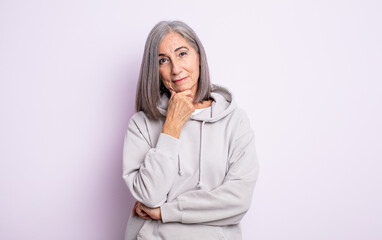 senior pretty woman looking happy and smiling with hand on chin, wondering or asking a question,...