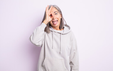 senior pretty woman smiling happily with funny face, joking and looking through peephole, spying on...