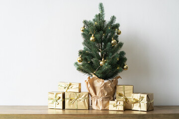 a small Christmas tree with warm bulbs in a pot on a wooden table with gifts wrapped in gold paper. the concept of Christmas