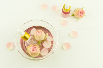 pink cosmetic water in a bowl with rose petals, dropper bottles with an extract of roses on a white background. top view.
