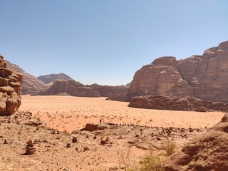 Fototapeta na wymiar Dans la zone protégée du désert de Wadi Rum en Jordanie, avec de hautes montagnes rocheuses, exploration dans l'inconnu, sous un soleil et forte chaleur, tas de rochers ou débris, vue sur le désert