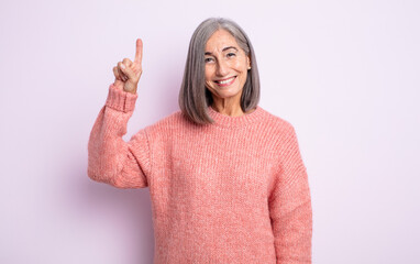 senior pretty woman smiling cheerfully and happily, pointing upwards with one hand to copy space