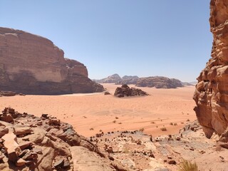 Fototapeta na wymiar Dans la zone protégée du désert de Wadi Rum en Jordanie, avec de hautes montagnes rocheuses, exploration dans l'inconnu, sous un soleil et forte chaleur, tas de rochers ou débris, vue sur le desert