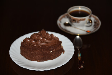 A piece of cake on a light plate with a cup of coffee and a beautiful spoon