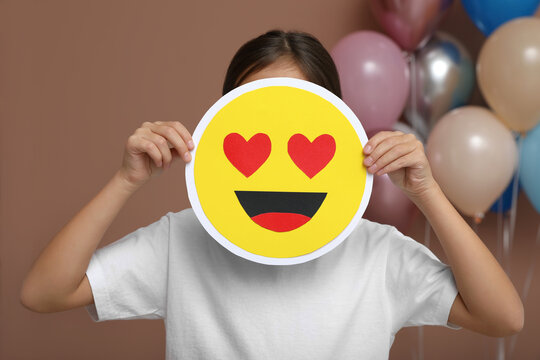 Little Girl Covering Face With Heart Eyes Emoji In Decorated Room