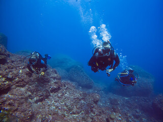 Group of scuba divers with bubbles. Diving in clear water. Rocks underwater. Underwater diving. Sardinia diving