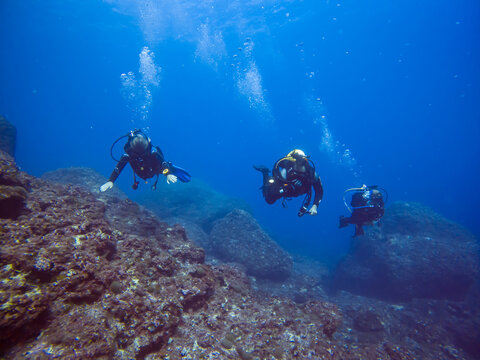 Group of scuba divers with bubbles. Diving in clear water. Rocks underwater. Underwater diving. Sardinia diving