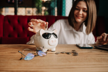 a business woman sits at a table in a cafe and collects coins in a piggy bank
