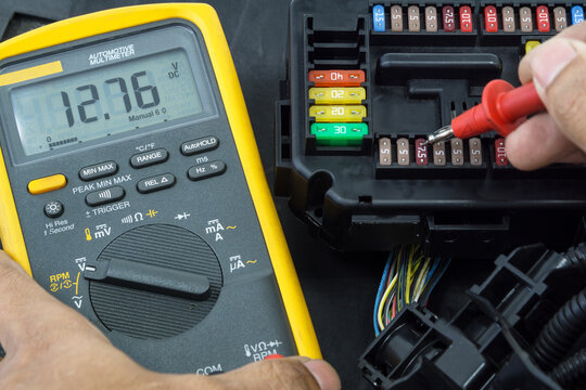 Selective focus an Auto mechanic using a multimeter voltmeter to check the voltage level of fuses in a car to check equipment malfunction in car electric system