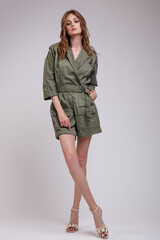 High fashion photo of a beautiful elegant young woman in a pretty green jumpsuit with patterns posing over white, soft gray background. Slim figure. Studio Shot.