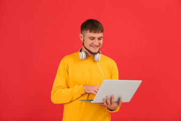 Young student with laptop and headphones on red background