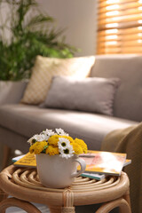 Cup with beautiful bright flowers and magazines on table in living room, space for text