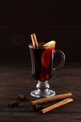 Mulled wine in a glass with orange and spices on a dark background.