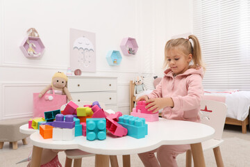 Fototapeta na wymiar Cute little girl playing with colorful building blocks at table in room, space for text
