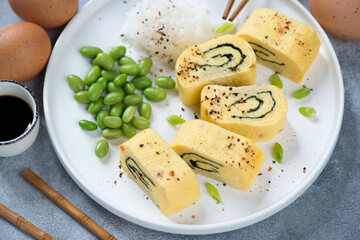 Round white plate with sliced japanese tamagoyaki, edamame beans, daikon and soy sauce, middle closeup, studio shot