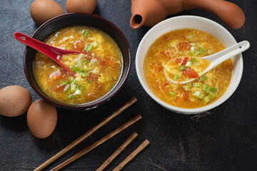 Bowls of chinese tomato egg-drop soup topped with scallions, elevated view on a dark-brown stone background, horizontal shot
