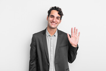 young businessman smiling happily and cheerfully, waving hand, welcoming and greeting you, or...