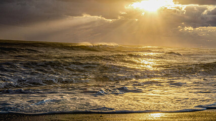 The rays of the setting sun flooded the sea. The sun breaks through the clouds in a sheaf. Golden path, splashes and foam of waves. Water is as heavy as mercury.