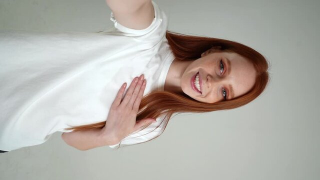 Vertical POV Portrait Of Cheerful Young Woman Talking Via Video Chat Using Mobile Phone Looking At Camera, On White Isolated Background In Studio. Point Of View Of Happy Lady Talking To Camera.