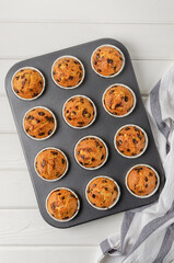 Ready muffins with chocolate chips in baking form on a white wooden background. Recipe step by step. Top view.