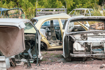 Fototapeta na wymiar Metal rusty different cars body parts abandoned in greenery. Car dump, wreck at a junkyard ready for recycling