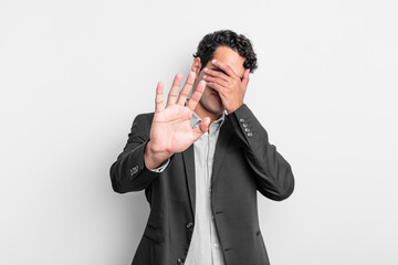 young businessman covering face with hand and putting other hand up front to stop camera, refusing...