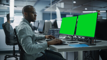 Multi-Ethnic Office: Black IT Programmer Working on Computer with Green Screen Chroma Key Display. Male Software Engineer Developing App, Program, Video Game. Terminal with Code Language.