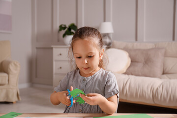 Little girl cutting color paper with scissors at table indoors