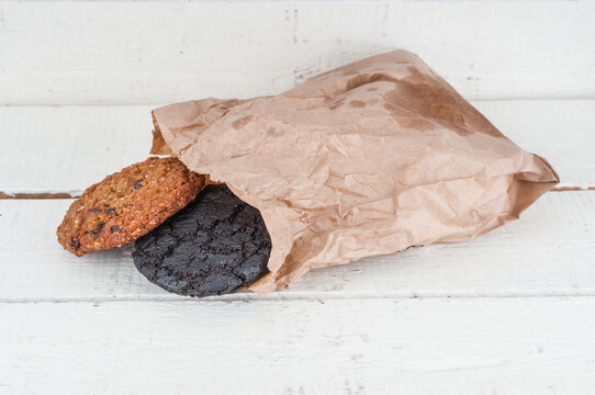 Brown and black cookies in paper packet on wooden background