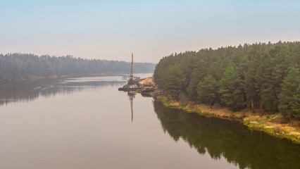 Obraz premium Floating crane on the river. Dredging crane working near shore. Conservation river flow. Nature, river, sky, clouds.