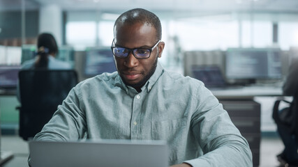 Modern Office: Portrait of Thoughtful Black IT Programmer Working on Laptop, Finding Solution, Solving Problems, Brainstorming. Male Software Engineer Wearing Glasses Develop App, Program, Video Game