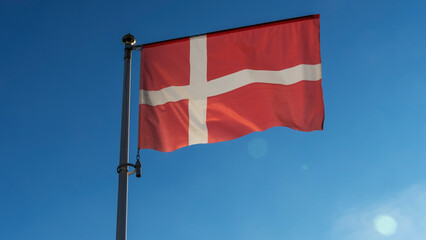 Flag of Denmark against the blue sky with sun rays and lens flare. Diplomacy concept. International relations.