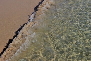 Above view over a diagonal segment of clear light green ocean wave water meeting a clean sandy beach