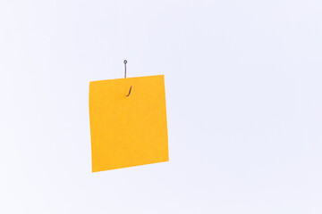 Mockup of a Blank Orange Memo Paper with Copy Space Hanging on a Fishing Hook Against the White Background. Reminder or To Do List. Sticky Note Template