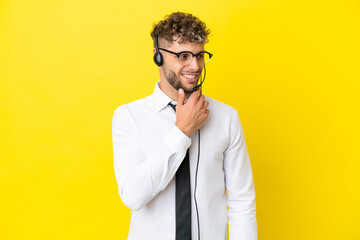 Telemarketer blonde man working with a headset isolated on yellow background looking to the side