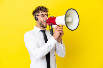 Telemarketer blonde man working with a headset isolated on yellow background shouting through a megaphone