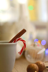 Cup of warm drink with candy cane and cinnamon stick, soft blanket and various Christmas decorations. Hygge at home. Selective focus.