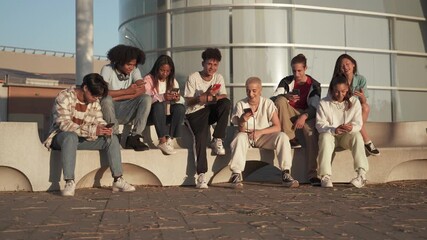 Multicultural group of teenager friends using cellphones and social media - Students sitting in modern urban area and typing on the smartphones
