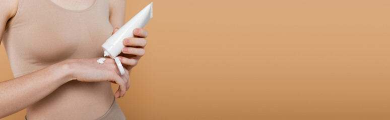 Cropped view of woman in top applying cream on hand isolated on beige, banner