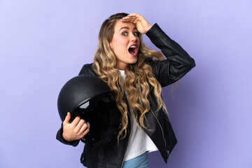 Young Brazilian woman holding a motorcycle helmet isolated on purple background doing surprise gesture while looking to the side