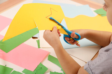 Little girl cutting color paper with scissors at table, closeup