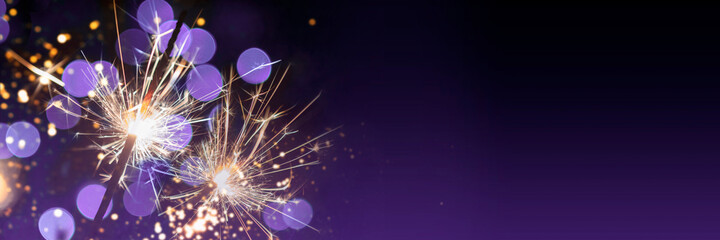 two classic sparklers with purple blurred bokeh lights on a black purple gradient background