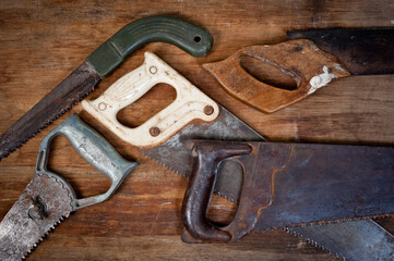 Old vintage metal saws for wood of different shapes and sizes, crumpled on a wooden background.