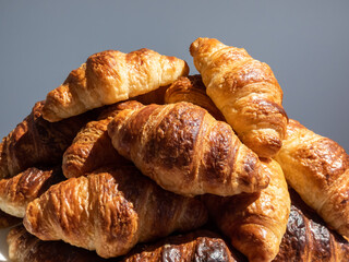 Pile of many fresh baked french croissants on white plate on white background in bright sunlight