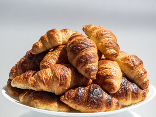 Pile of many fresh baked french croissants on white plate on white background in bright sunlight
