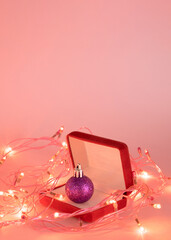 Christmas violet bauble in open ring box with New Year's lights.Surprise holiday gift concept on a soft pink background.Aesthetic design